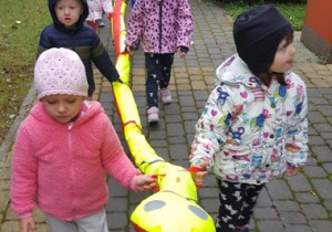 Dzieci idą z wężem na przedszkolny plac zabaw.
